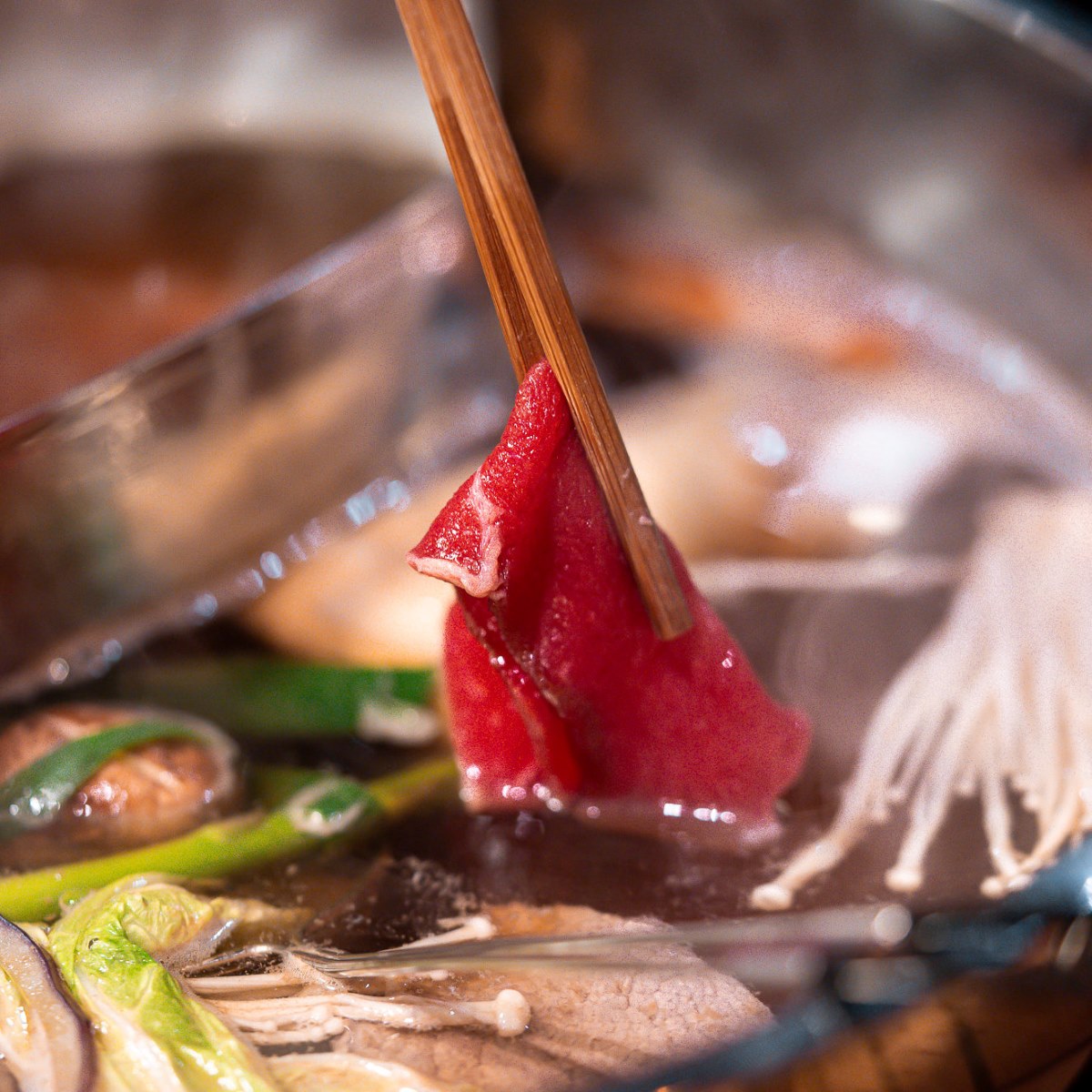 Scheibe Rindfleisch an Holzstäbchen über dem heißen Shabu-Shabu-Sud mit Enoki-Pilzen und Lauch