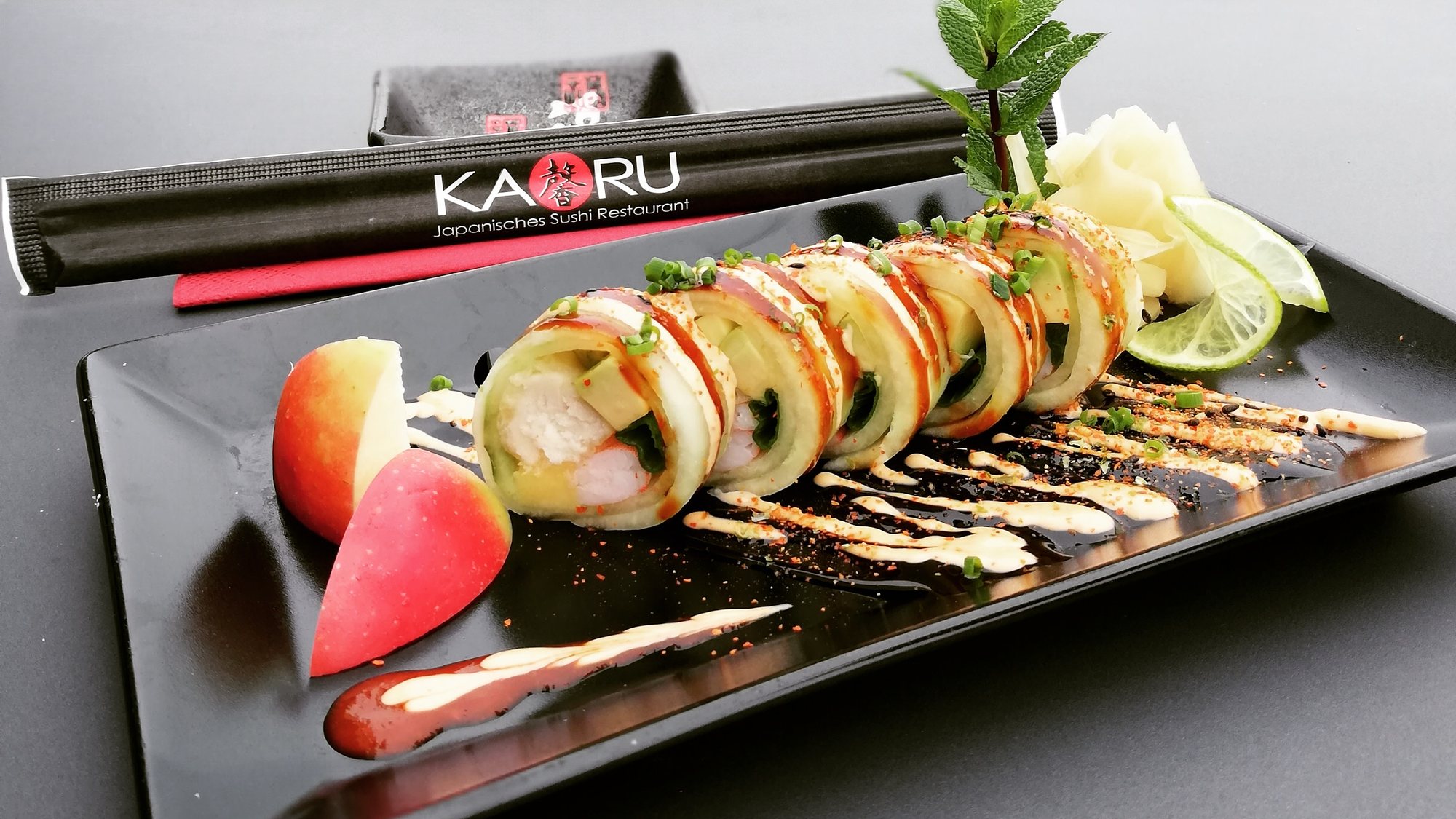 Sushi-Rolle im Gurkenmantel mit Apfelspalten und Limette auf schwarzer Platte im KAORU